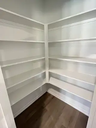 Model Home A built-in pantry with white shelving and hardwood flooring, offering ample storage.