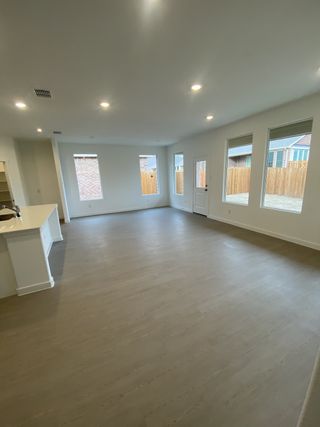 A spacious, open-plan living area with wood flooring, large windows, and modern recessed lighting.