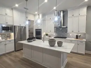 A modern kitchen with white cabinetry, a marble island, pendant lights, and stainless steel appliances.