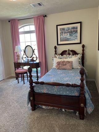 A cozy bedroom with a vintage wooden bed, floral bedding, pink curtains, and a classic vanity table.