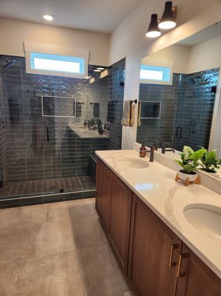 Elegant bathroom with dual vanities, glossy tiled shower, and warm wood cabinetry.