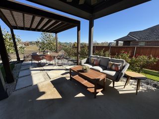 A cozy patio with cushioned seating and a dining area under a pergola, surrounded by greenery and sunshine.