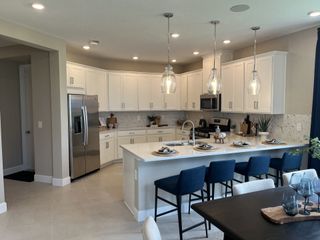 A modern kitchen with white cabinetry, sleek appliances, glass pendant lights, and a spacious island with seating.