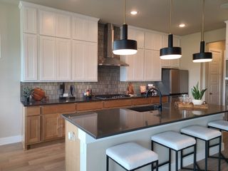 Model Home A modern kitchen featuring sleek black countertops, white and wood cabinetry, and stylish pendant lighting.