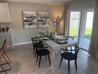 Model Home A modern dining room with a sleek white table, black chairs, abstract art, and large sliding doors opening to a grassy view.