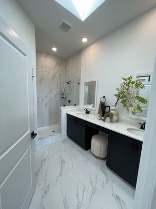Elegantly designed bathroom featuring marble-patterned tiles, dual sinks with black cabinetry, and a glass-enclosed shower.