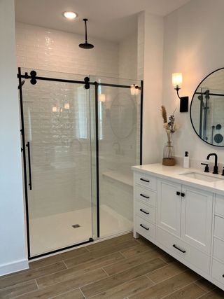 A chic bathroom featuring a glass-enclosed shower, elegant white vanity, and natural accents on tiled floors.