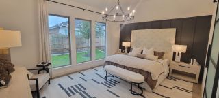 Model Home A cozy bedroom with a tufted headboard, elegant chandelier, and large windows overlooking a lush garden.