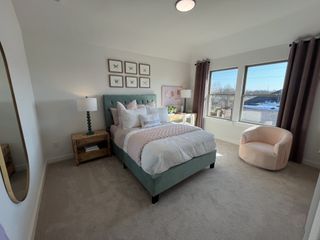 A cozy bedroom with a tufted green bed, soft pink accents, and large windows for natural light.