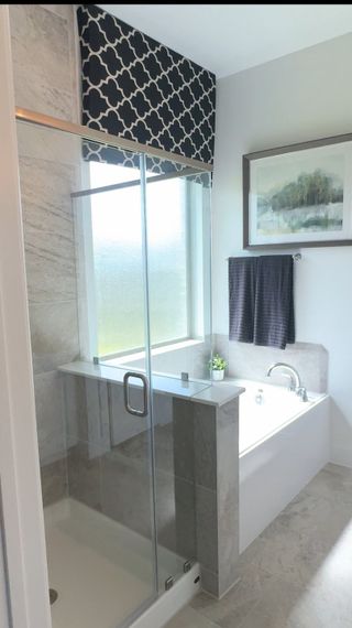 Model Home A modern bathroom with a glass shower, tiled bathtub, and elegant decor, featuring a stylish window treatment.