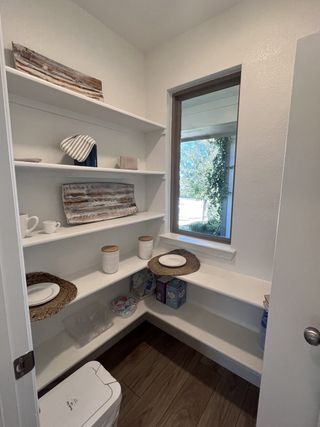 Model Home A cozy pantry with wooden shelves, natural light from a small window, and neatly placed dishware for a functional touch.