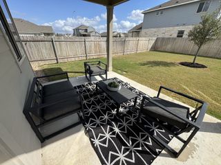 Model Home A cozy patio with modern seating, a stylish black-and-white rug, overlooking a spacious fenced yard.