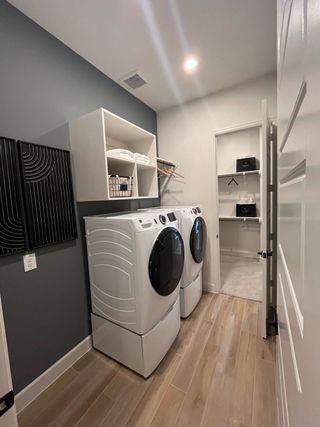 A modern laundry room with sleek appliances, wooden flooring, open shelving, and ample lighting.