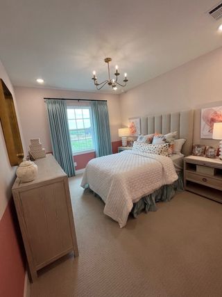A cozy bedroom with soft pink walls, elegant chandelier, plush headboard, and stylish decor, creating a serene ambiance.
