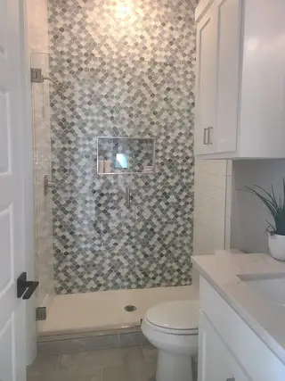 Model Home A modern bathroom featuring a mosaic tile shower, sleek vanity, and elegant gray flooring.