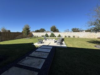 A serene backyard with a stone patio, fire pit, and lush lawn at 6 Creeks by Perry Homes (Kyle, TX).