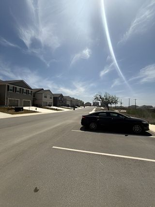 Street view A sunny street in Magnolia Village (San Antonio, TX) by Rosehaven Homes features a parked black car and modern townhomes under a bright sky.