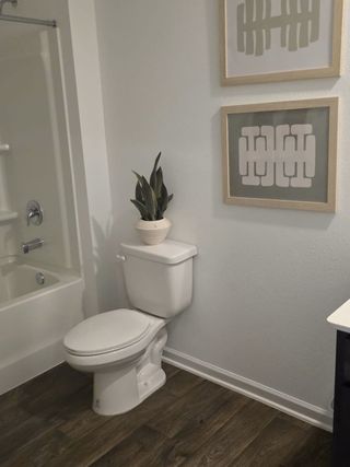 Model Home A modern bathroom features wood flooring, abstract art, and a sleek white toilet with chic decor accents.