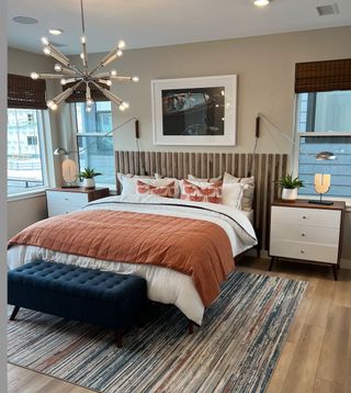 A modern bedroom featuring a tufted bench, geometric lighting, a textured rug, and a cozy warm duvet.