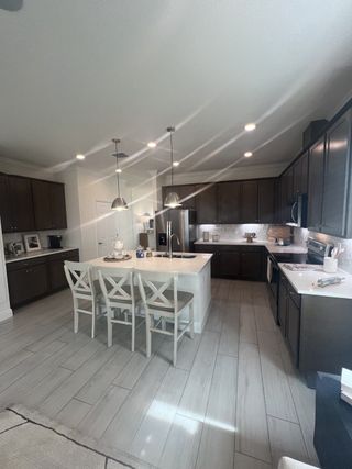 Model Home A modern kitchen featuring dark cabinets, an island with seating, pendant lights, and sleek appliances.