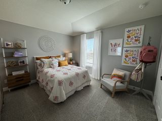 A cozy bedroom with patterned bedding, wall art, and neutral tones. Features include a comfy chair and decorative shelving.