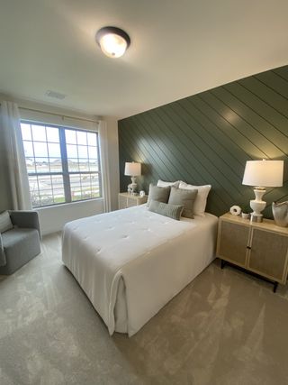 Model Home A modern bedroom with a dark green accent wall, stylish decor, and a large window bringing in natural light.
