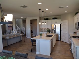 A modern kitchen with sleek white cabinetry, pendant lighting, and a spacious island, opening to a cozy living area.