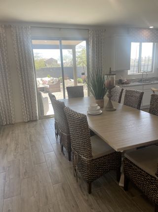 A bright dining area with wicker chairs, a large table, and natural light streaming in through sliding glass doors.