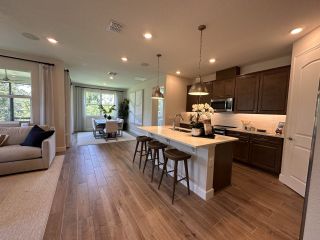 Model Home A modern kitchen with dark cabinets, white countertops, and an open layout leading to a bright dining area and cozy living room.