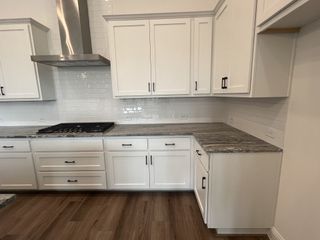 A modern kitchen with sleek white cabinets, a stainless steel range hood, and patterned countertops.