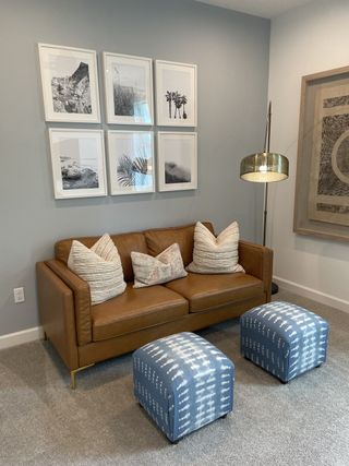A cozy lounge with a brown leather sofa, patterned cushions, blue ottomans, and artistic wall decor.