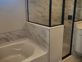 A luxurious bathroom with a marble-tiled bathtub, sleek glass shower, and modern fixtures.