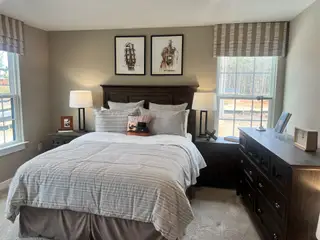 A cozy bedroom with striped bedding, wooden furniture, and natural light from large windows. Elegant decor and warm tones.