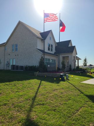 Street view A charming brick home with manicured lawn and flag display in Painted Tree 50' Series by Southgate Homes (McKinney, TX).
