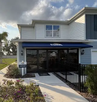 A welcoming sales office with coastal-inspired blue and white siding and a charming awning in Emerald Pointe by Pulte Homes (Apopka, FL).