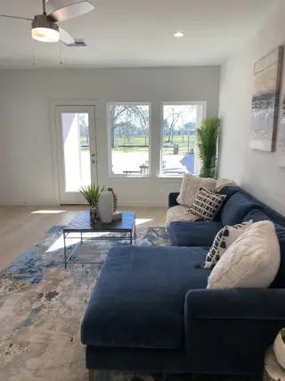 A cozy living room featuring a plush blue sectional, abstract rug, and abundant natural light through large windows.