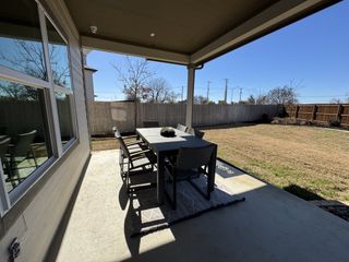A cozy covered patio with a dining set overlooks a fenced backyard, perfect for outdoor gatherings.