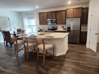 A modern kitchen with dark wood cabinets, a large island, stainless steel appliances, and sleek dining area.