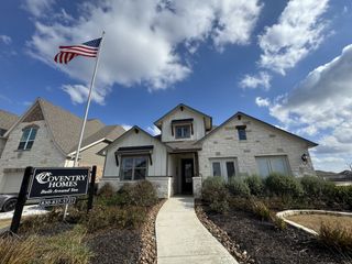 A charming white stone and board-and-batten home with lush landscaping in Overlook at Creekside by Coventry Homes (New Braunfels, TX).