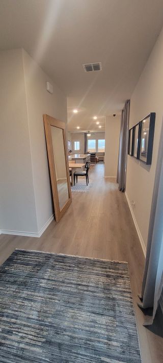 A modern hallway with wood flooring, a large mirror, and elegant lighting leading to an open-concept living area.