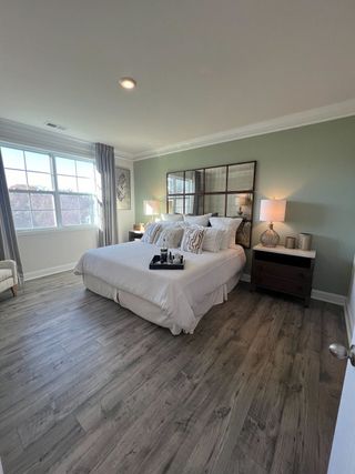 A cozy bedroom featuring hardwood floors, a large window, serene green walls, and tasteful decor with modern furnishings.