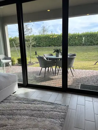 A cozy patio view with wicker chairs on a brick path, framed by sliding glass doors and soft rug flooring.