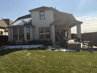 A spacious backyard with a covered patio, fire pit, and lush green lawn in The Parks at Wilson Creek by Highland Homes (Celina, TX).
