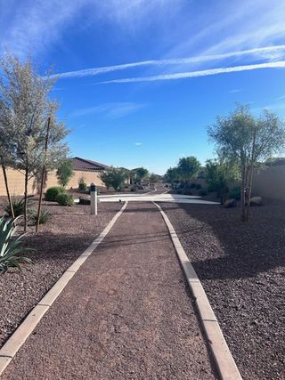 A serene pathway lined with desert landscaping under a bright blue sky in Ventana de Estrellas Traditions by KB Home (Goodyear, AZ).