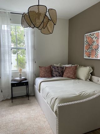 A cozy bedroom featuring a stylish pendant light, neutral tones, and patterned cushions on a plush daybed.