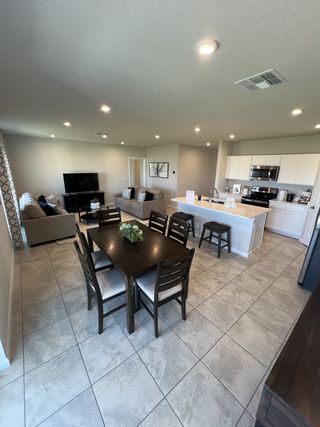 Model Home A spacious open-plan living area with tiled floors, a modern kitchen, cozy seating, and a stylish dining table.