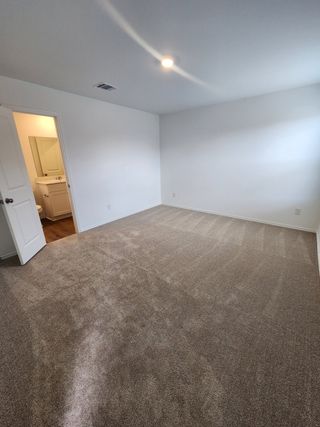 Model Home A spacious room with plush carpet, white walls, recessed lighting, and an adjacent bathroom for convenience.