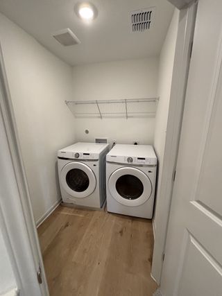 A modern laundry room with wood floors and Samsung washer-dryer units in Blue Ridge Ranch by Rosehaven Homes (San Antonio, TX).