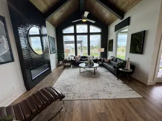 Model Home A chic living room with a vaulted ceiling, sleek fireplace, large windows, and cozy seating. Perfect for relaxation and entertaining.