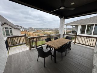A covered outdoor patio with wood flooring, cozy seating, and scenic views in Veramendi by Perry Homes (New Braunfels, TX).